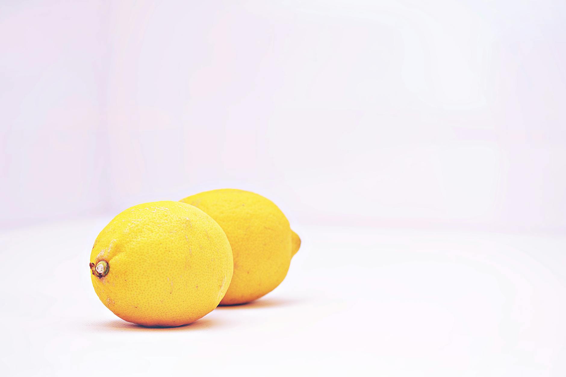 Two vibrant lemons on a minimalistic white background, symbolizing freshness and sensuality.