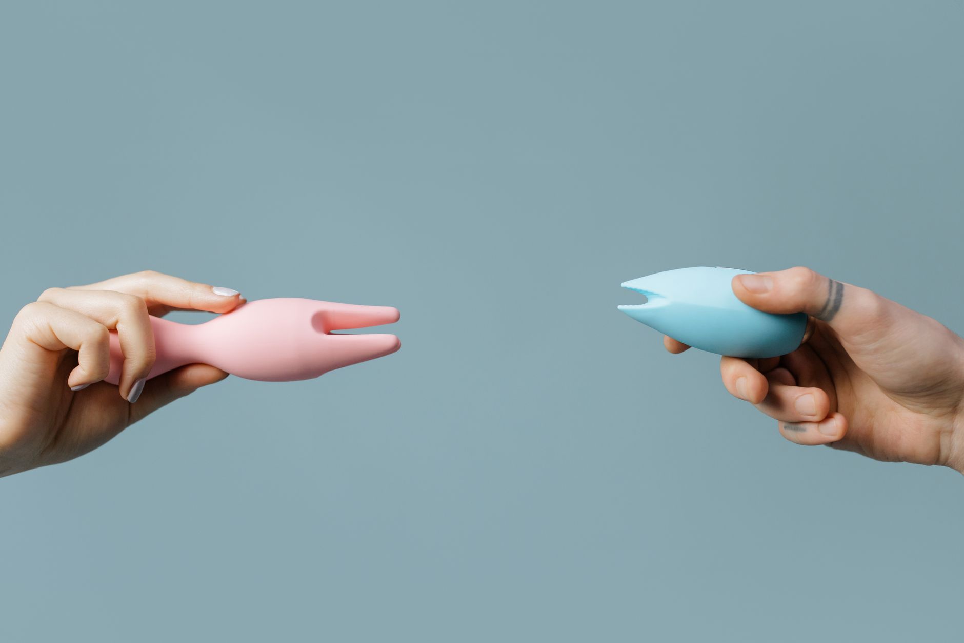 Close-up of a hand holding a modern orange vibrator against a minimalistic purple backdrop