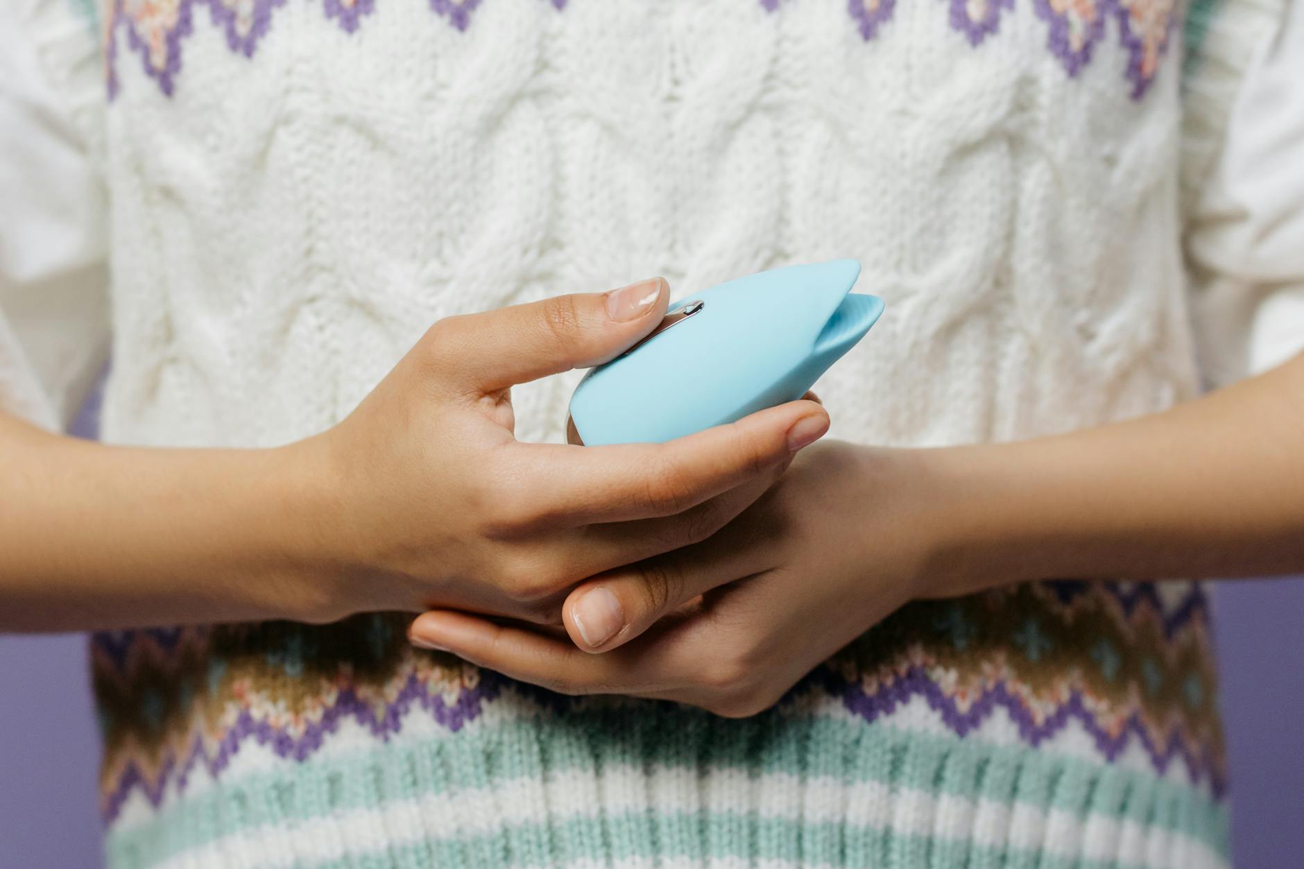 Close-up of hands holding a lemon vibrator against a knitted sweater.